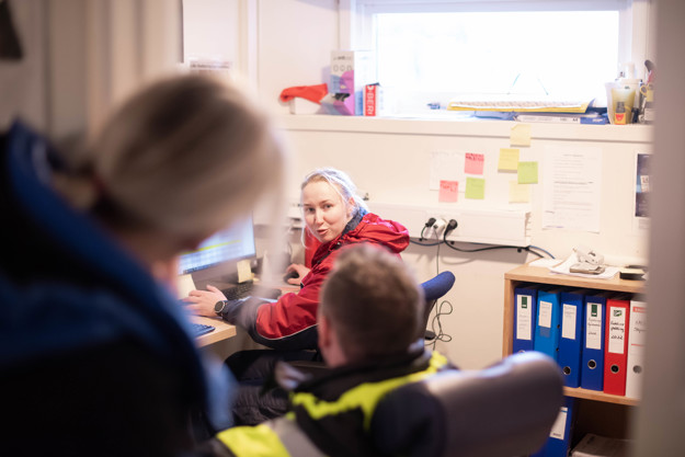 To mennesker ser inn på Agnete som sitter foran PCen og jobber på kontoret sitt.